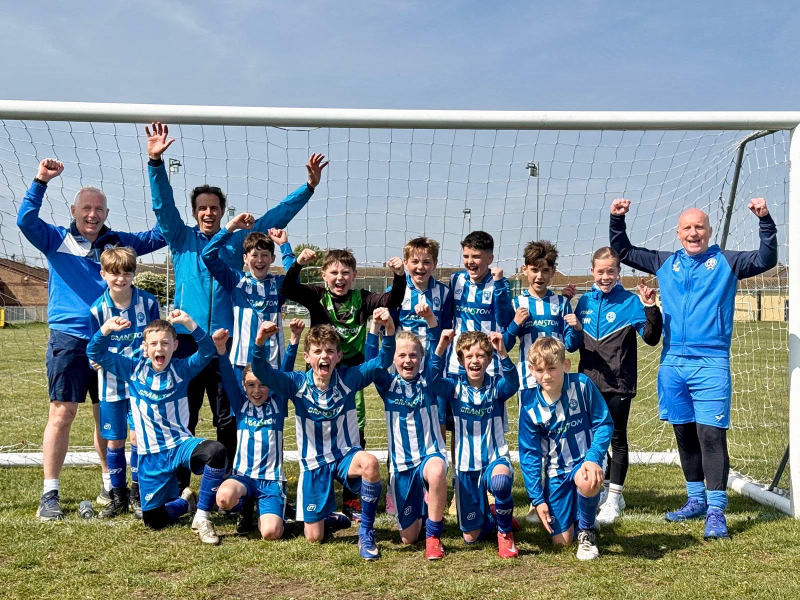 Players and coaches celebrating at the goal in blue and white FT teamwear