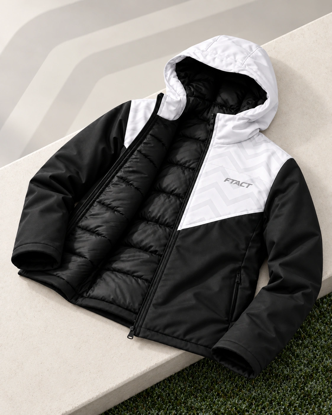 Black and white FTACT hybrid coat resting on a pale bench beside damp grass